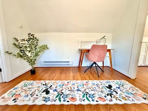 A room with a wooden floor, a desk with a chair, a potted plant, and a floral rug. - Spacious Peaceful Redding Cottage Retreat (Redding)