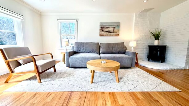 Ein modernes Wohnzimmer mit Sofa, Sessel und Couchtisch, einem Kamin und einem Fenster.