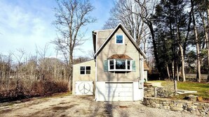 Ein zweistöckiges Haus mit Garage, umgeben von einer Schotterauffahrt und einer Steinmauer.