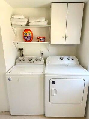 A laundry area with two white washing machines, a shelf with Tide detergent, and a cabinet. - Spacious Peaceful Redding Cottage Retreat (Redding)