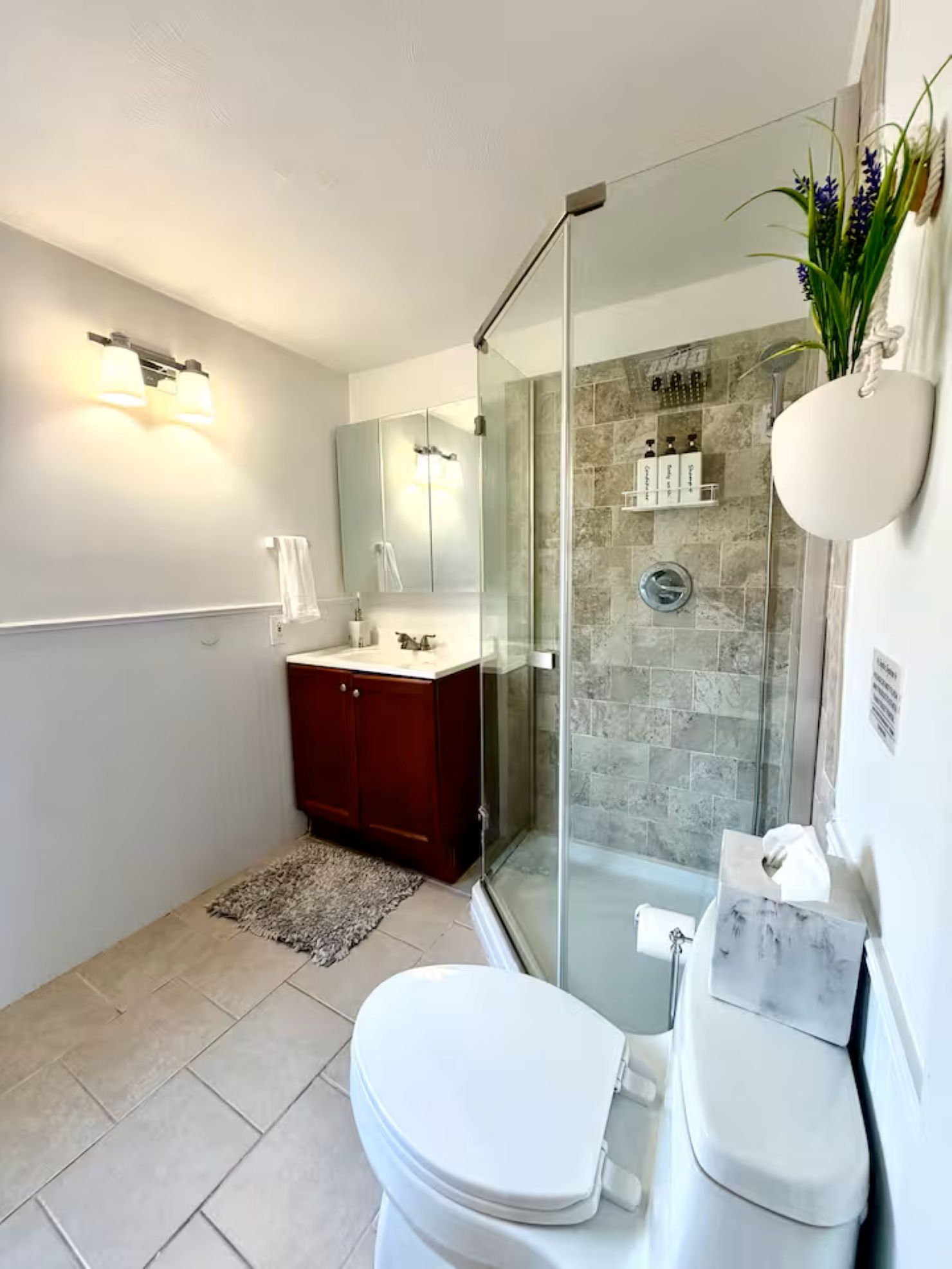 A modern bathroom with a glass shower enclosure, a white toilet, a vanity with a mirror, and a showerhead.
