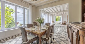 A dining area with a checkered floor, a wooden table set for four, and large windows with a view of greenery. - Les Tolets (Cancale)