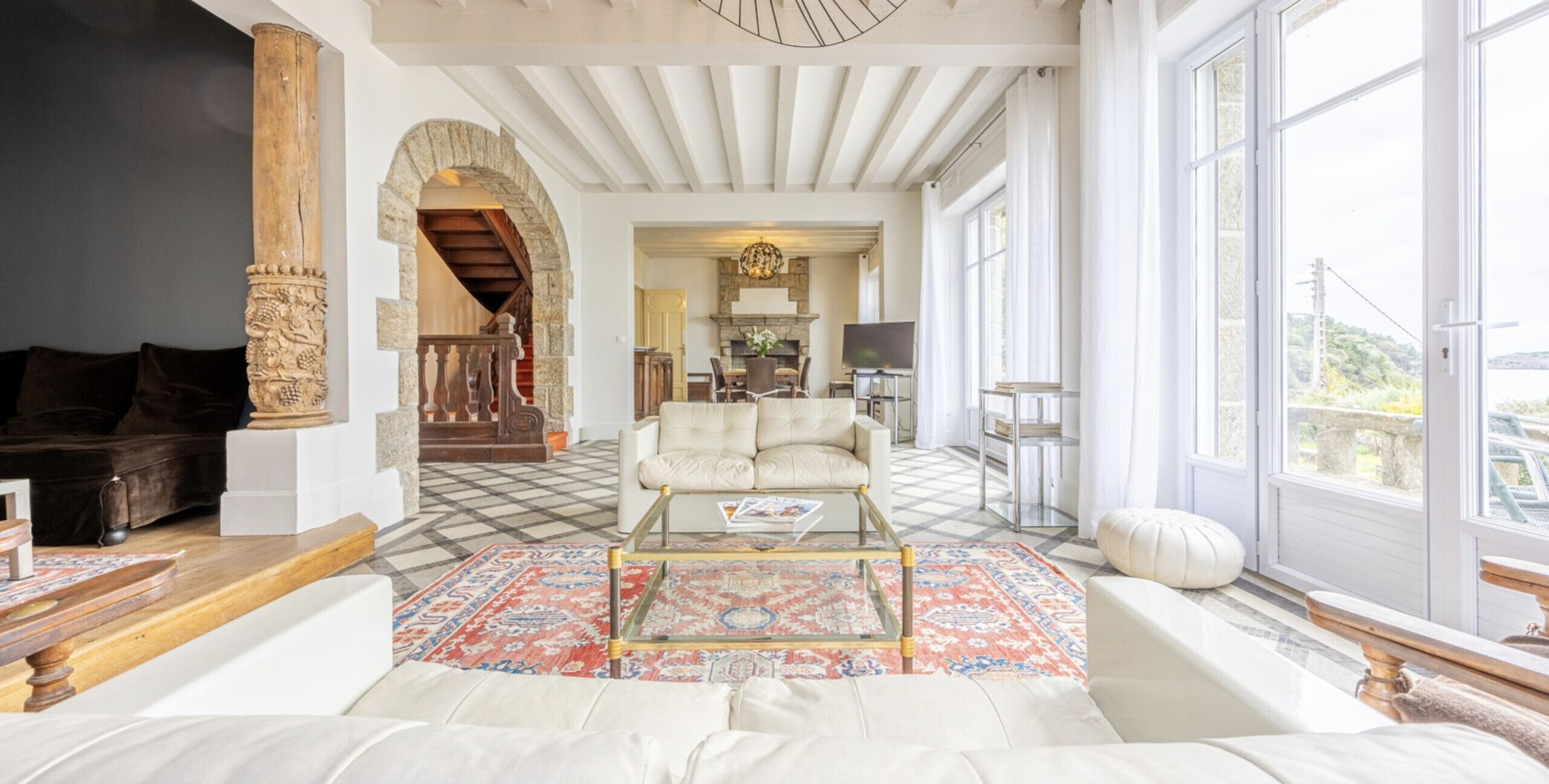 A spacious living room with a checkered floor, a white sofa, a coffee table, and a large window offering a view of the outdoors.