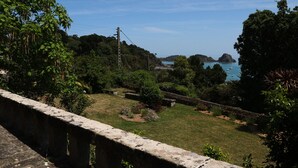 Eine Küstenlandschaft mit einer Steinbrücke, üppigem Grün und Blick auf das Meer mit Booten.