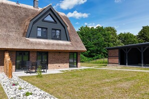 Une maison moderne avec un toit de chaume, une façade en briques et un espace extérieur aménagé avec des sièges.