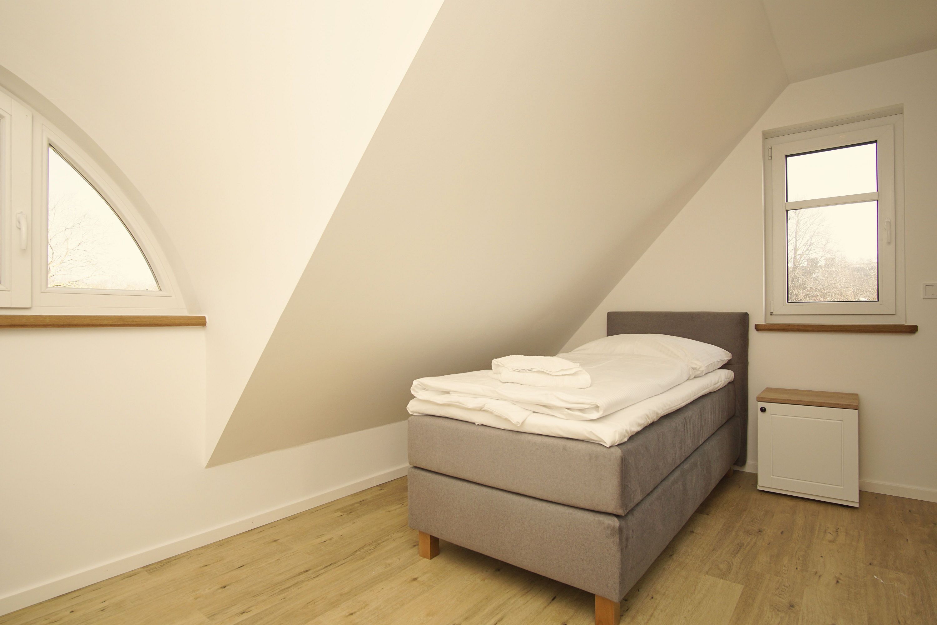 Une chambre à coucher avec un lit, une petite table de chevet, une fenêtre et un plafond en pente.