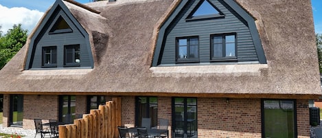 A modern house with a thatched roof, brick exterior, and a patio with outdoor furniture.