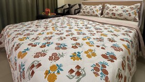Een slaapkamer met een bloemenprint sprei, een nachtkastje, een lamp en een stoel.