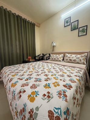 Un dormitorio con edredón estampado, una mesita de noche, una lámpara y una silla.
