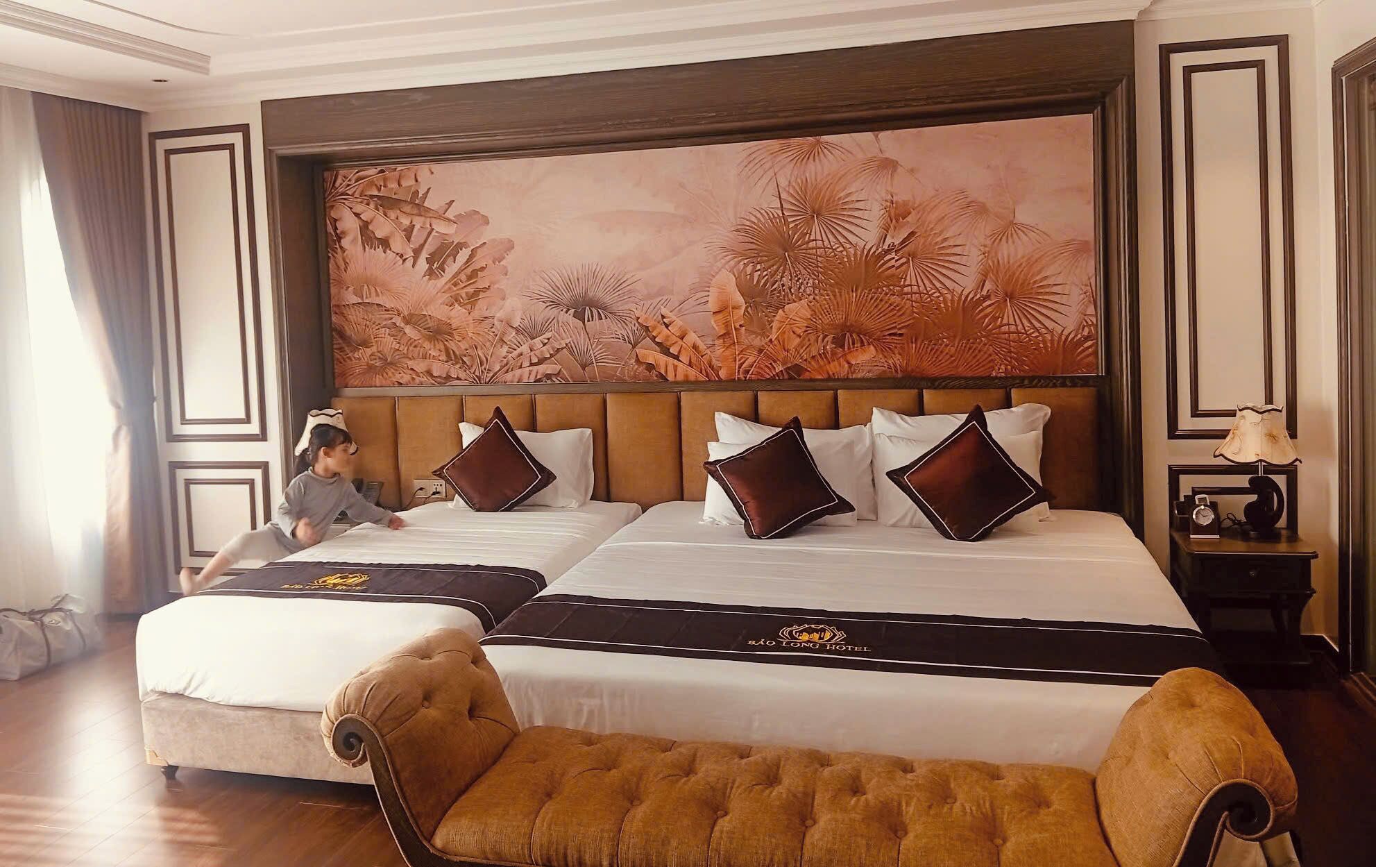 A hotel room with a large bed, two pillows, a headboard, a nightstand, a lamp, and a large floral wall mural.