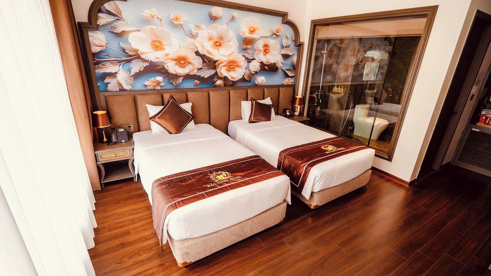 Quarto de hotel com duas camas, um grande mural floral, uma porta de vidro deslizante e piso de madeira.