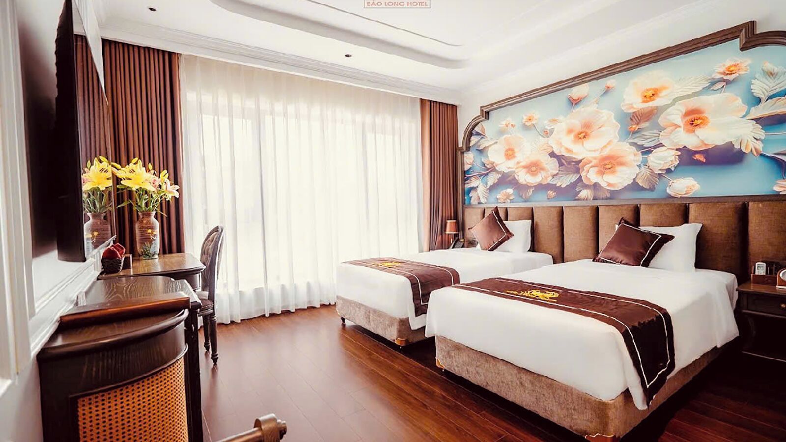 Habitación de hotel con dos camas, un escritorio, una silla, un cuadro floral grande y vistas al exterior.
