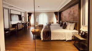 Habitación de hotel con una cama grande, un escritorio, una silla, un televisor y un espejo.
