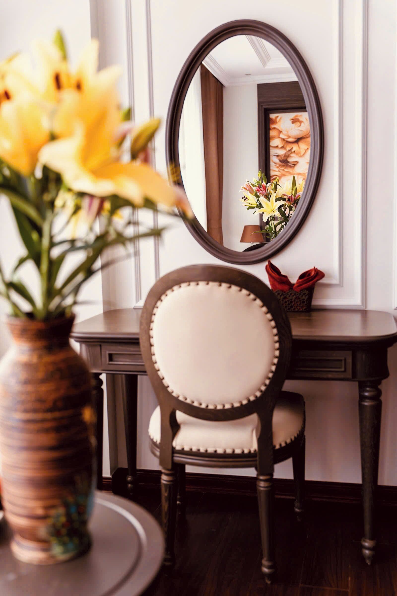 Una habitación con una mesa redonda, una silla, un espejo y un jarrón con flores.