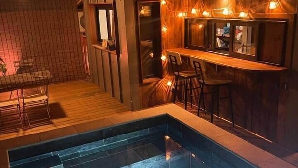 Ein Pool mit Stufen, einer Holzterrasse und einem Barbereich mit Stühlen.