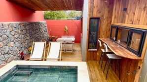 Ein Poolbereich mit Holzterrasse, Steinmauer und Barbereich mit Hockern.