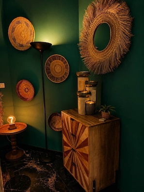 Una stanza con una parete verde, un armadietto in legno, una lampada da terra e diverse decorazioni murali intrecciate.