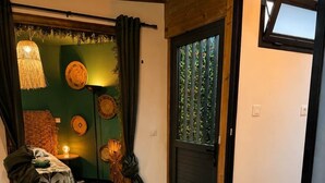 A room with a round wooden table, a chair, a bed with a green wall and a window, and a door with a window. - Tiny house with private Jacuzzi (Saint-Paul)