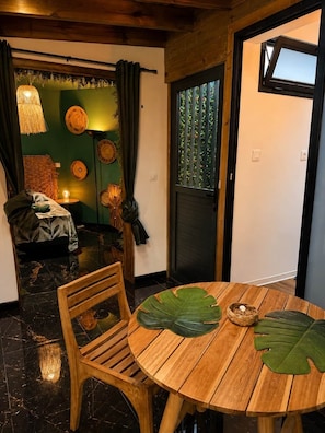 Une pièce comprenant une table ronde en bois, une chaise, un lit avec un mur vert et une fenêtre, ainsi qu’une porte dotée d’une fenêtre.