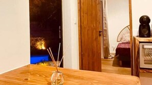 A room with a wooden table, a small vase with sticks, a bed with a red blanket, a fan, and a coffee machine. - Tiny house boucan with pool (Saint-Paul)