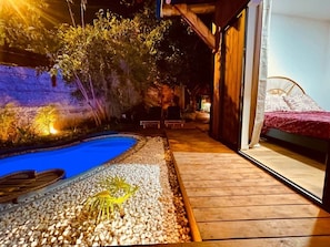 Una piscina con muelle de madera, cama y zona de estar cubierta.