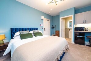 A bedroom with a bed, bedside table, and a kitchenette area. - The Station at Shustoke (Birmingham)