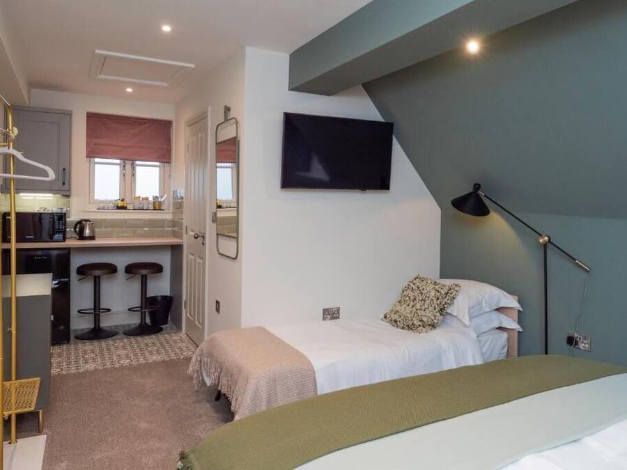 Un dormitorio con cama, mesita de noche y televisor montado en la pared.