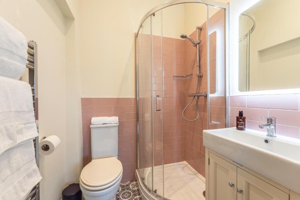 A bathroom with a glass-enclosed shower, a toilet, a sink with a mirror, and a towel rack.