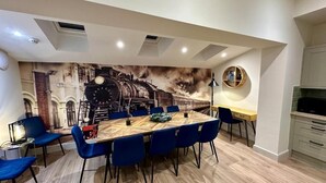 Un comedor con una mesa grande, sillas azules, un mural de un tren y una cocina moderna al fondo.