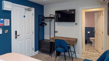 Ein Zimmer mit einem Bett, einem Schreibtisch, einem Stuhl, einem Fernseher und einer Tür zu einem Badezimmer.