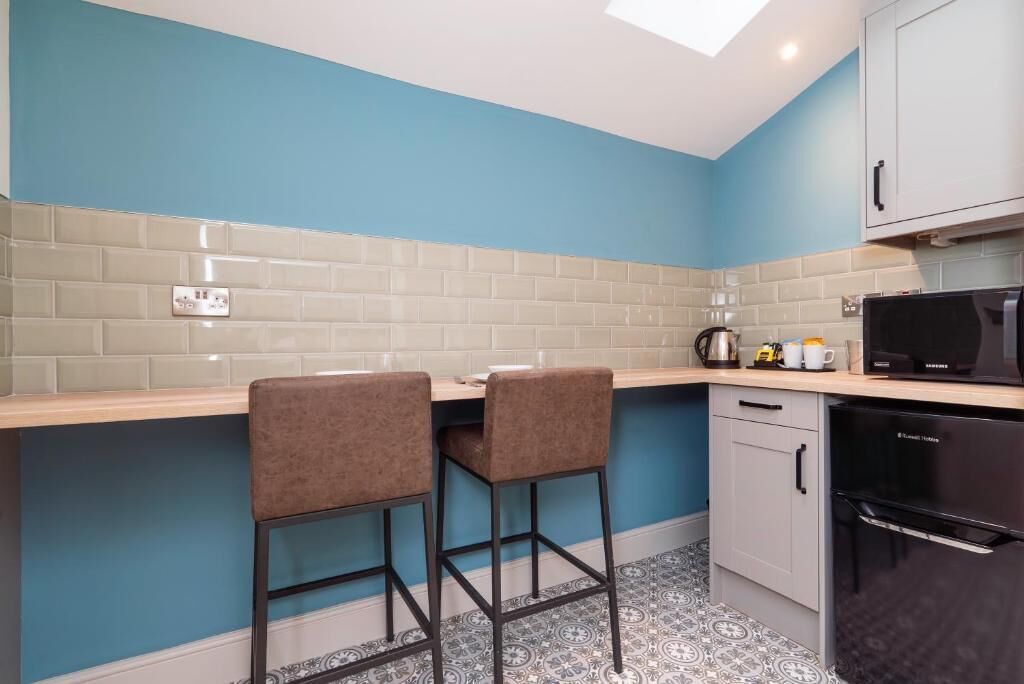 A kitchen with two bar stools, a microwave, a dishwasher, and a tiled backsplash.
