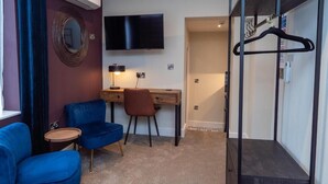 Habitación de hotel con escritorio, dos sillas, televisor, espejo y perchero.