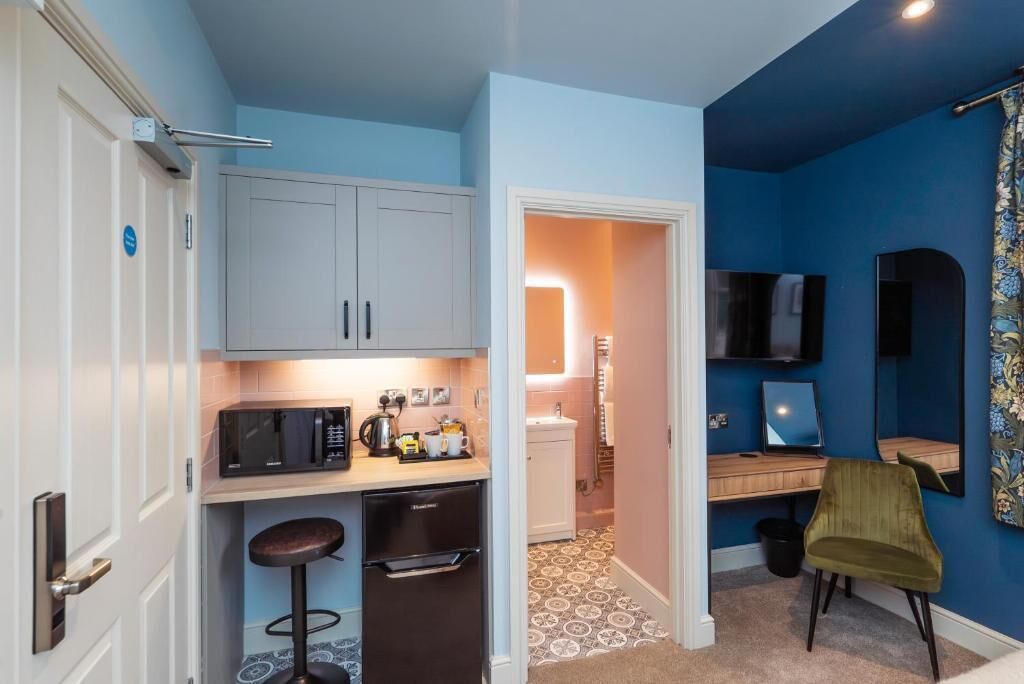 A compact kitchen with a microwave, kettle, and bar stools, leading to a bathroom with a sink and toilet.