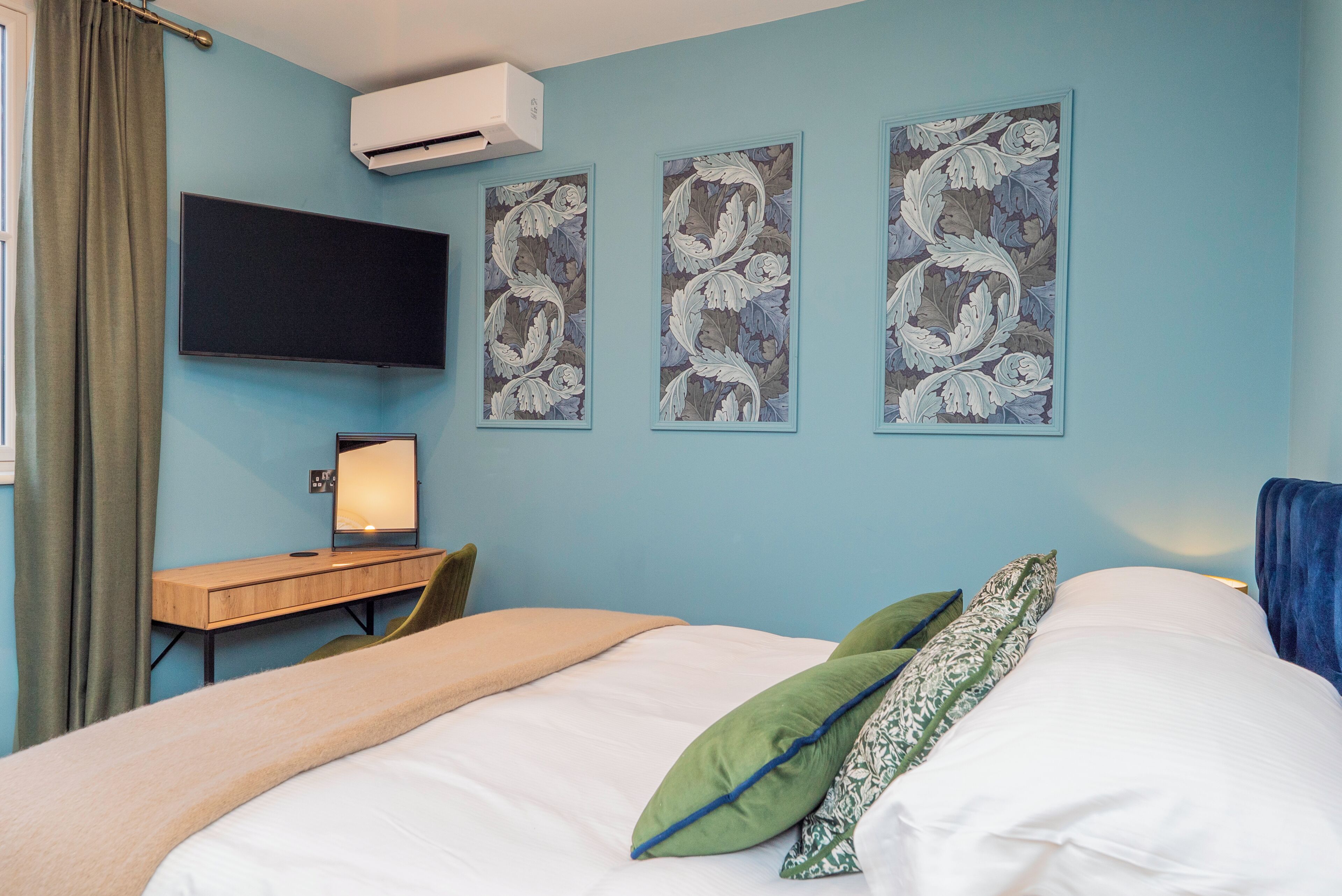 A bedroom with a bed, a desk, a chair, a flat-screen TV, and three floral wall art pieces.