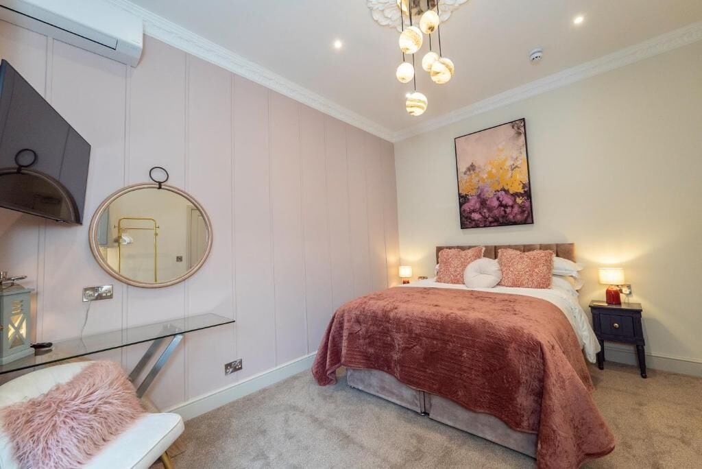A bedroom with a bed, bedside tables, a mirror, a chandelier, and a painting on the wall.