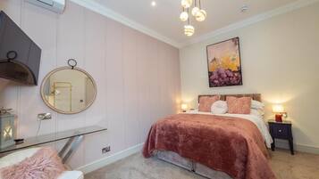 A bedroom with a bed, bedside tables, a mirror, a chandelier, and a painting on the wall.