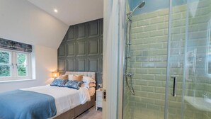 Un dormitorio con cama, mesita de noche y zona de ducha con mampara de vidrio.