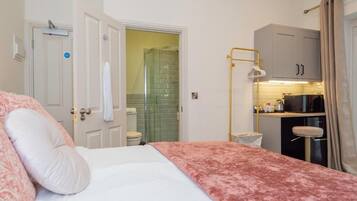 A hotel room with a bed, a shower, a kitchenette, and a door leading to another room.