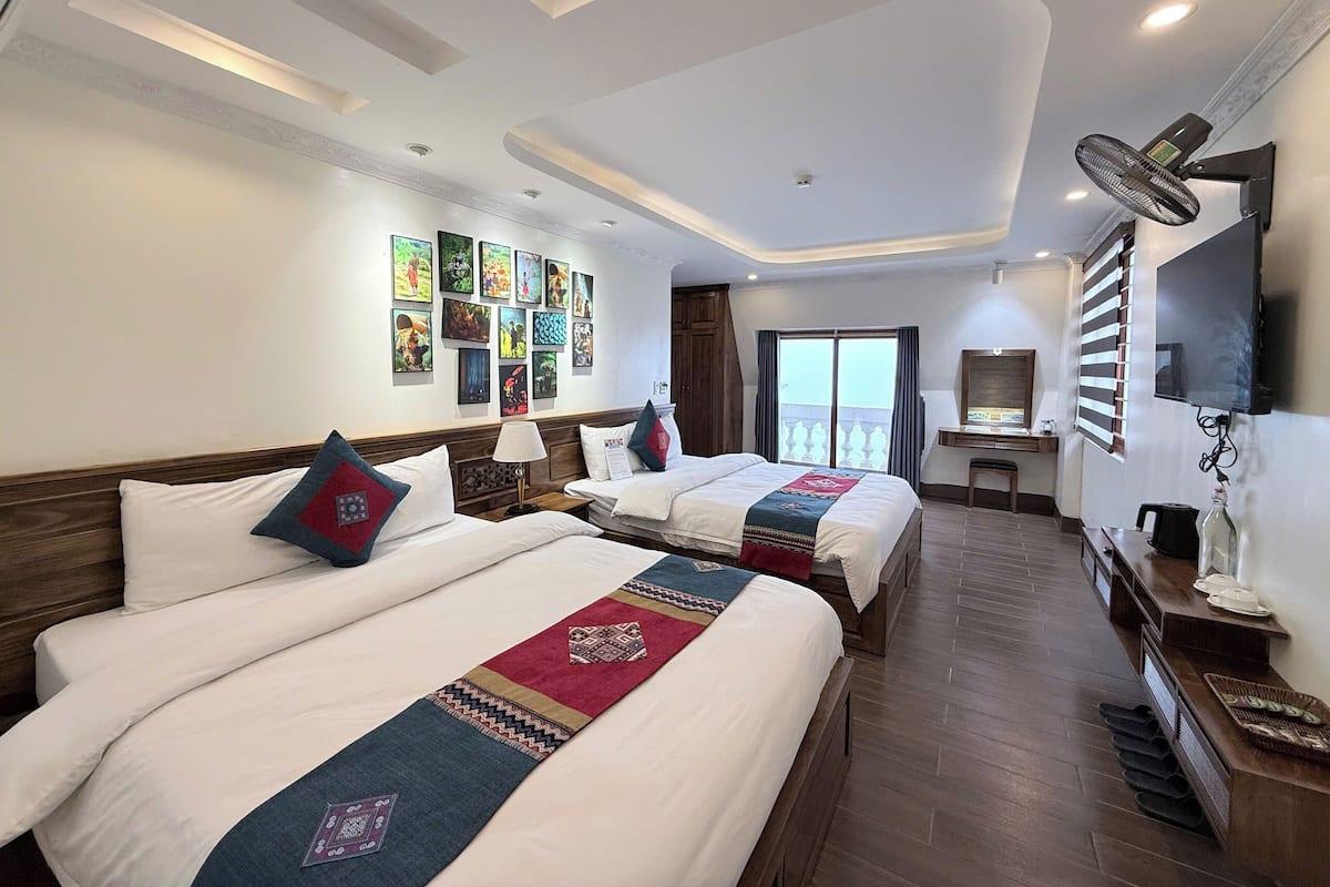 Habitación de hotel con dos camas, televisión, escritorio y obras de arte en la pared.