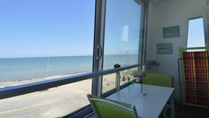 A room with a large window overlooking the sea, a table with chairs, and two wall-mounted pictures. - Window overlooking the sea, loggia overlooking the sea on the beachfront (Courseulles-sur-Mer)