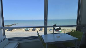 A room with a large window overlooking a beach, a table, and a chair. - Window overlooking the sea, loggia overlooking the sea on the beachfront (Courseulles-sur-Mer)