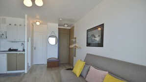 A modern living room with a grey sofa, yellow cushions, a framed picture, and a kitchen area with white cabinets and a hanging mirror. - Window overlooking the sea, loggia overlooking the sea on the beachfront (Courseulles-sur-Mer)