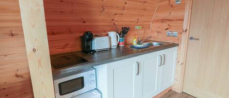 A compact kitchen with wooden walls, a microwave, a toaster, and a sink.