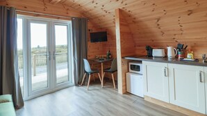 A wooden cabin interior with a dining area, kitchen, and sliding glass doors to an outdoor deck. - Douglas (Stranraer)