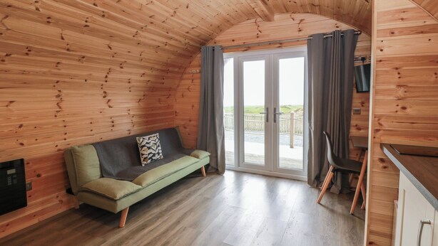 A cozy cabin interior with a wooden ceiling, a sofa, a sliding glass door to the outside, and a kitchenette. - Douglas (Stranraer)