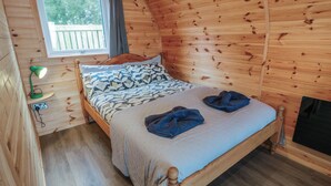A cozy wooden cabin room with a bed, a window, and a small desk with a lamp. - Douglas (Stranraer)