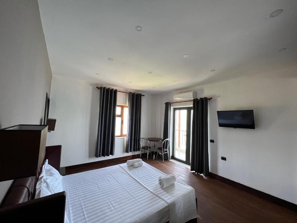 Ein Hotelzimmer mit Bett, Schreibtisch, Stuhl und einem an der Wand befestigten Fernseher.