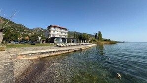 Un hôtel situé au bord de l’eau, doté d’une piscine, offrant une vue sur la mer et s’inscrivant dans un paysage montagneux.