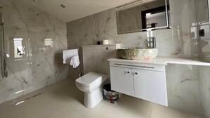 Une salle de bain avec un mur en marbre, des toilettes, un lavabo avec un grand miroir et une douche.