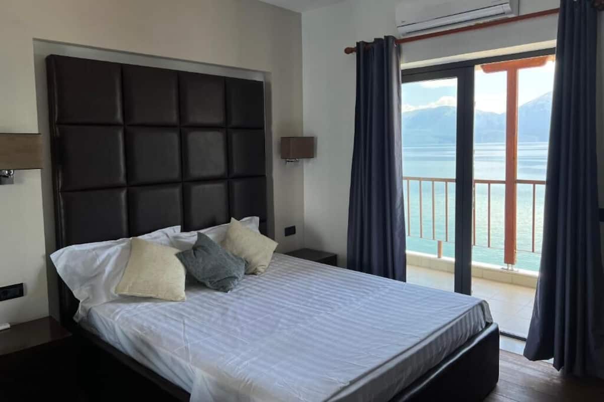 Ein Schlafzimmer mit einem großen Bett, einem Kopfteil, einem Nachttisch, einer Klimaanlage und Meerblick vom Balkon.